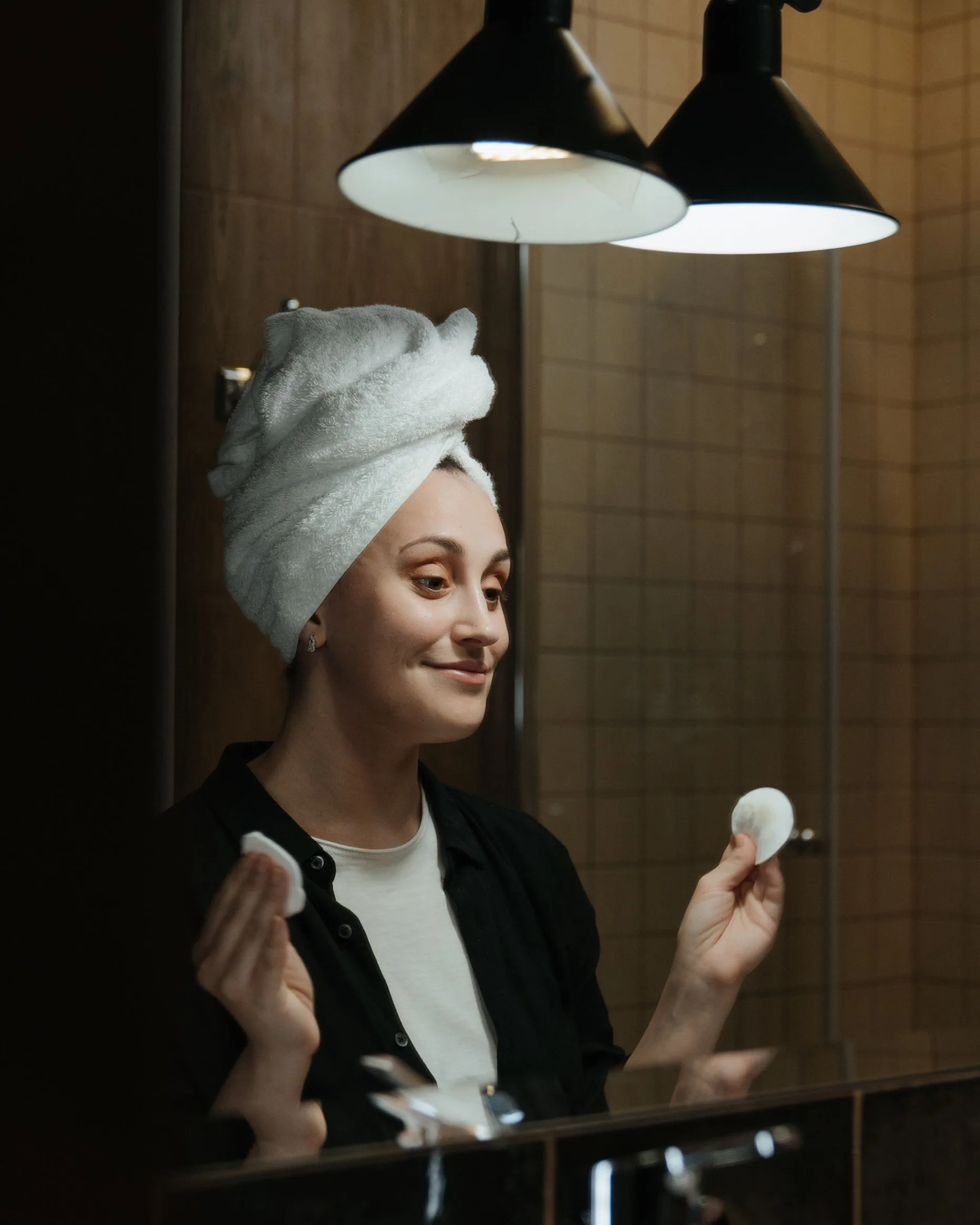 Une femme, une serviette sur les cheveux, applique un coton sur sa joue